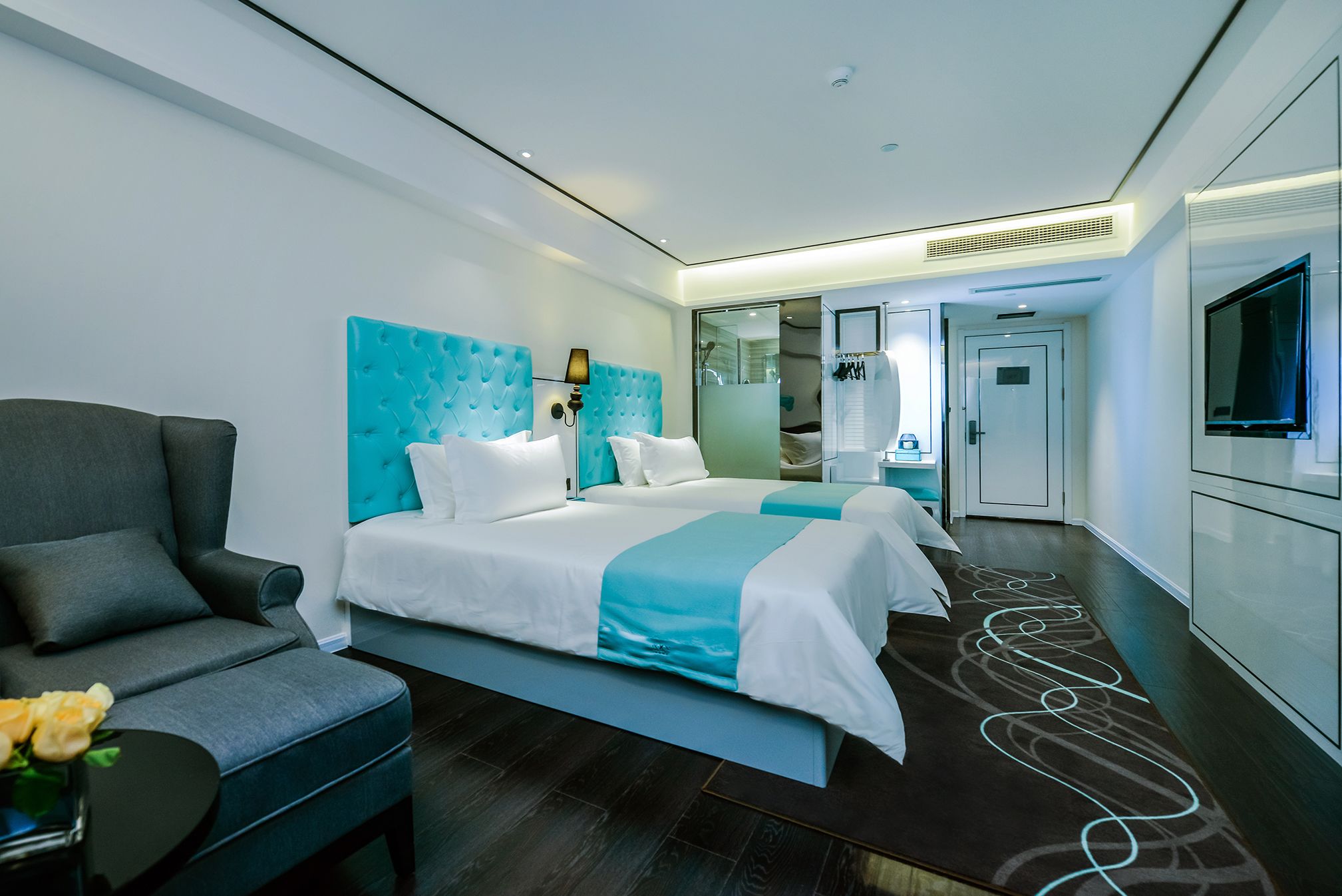 A modern hotel room with a large bed, a sofa, a TV, and a bathroom visible through an open door.