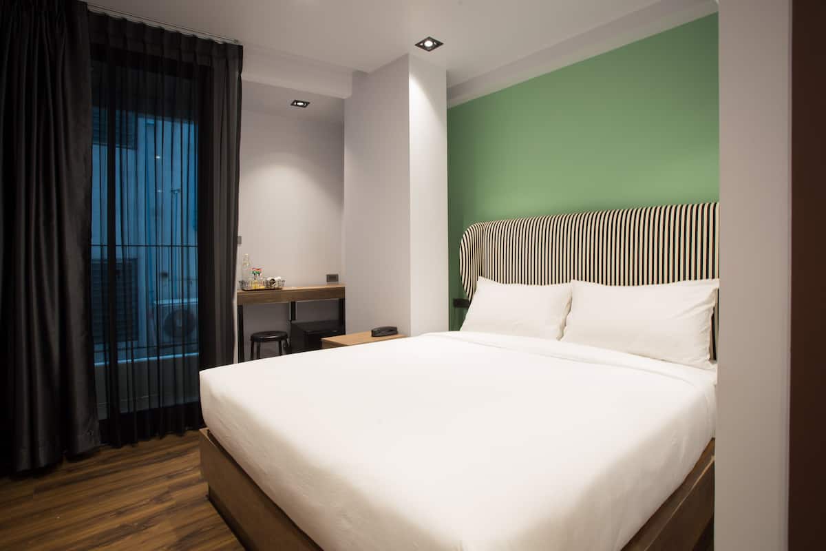 Una habitación de hotel con una cama grande, un escritorio con silla, una mesita y una ventana con cortinas.