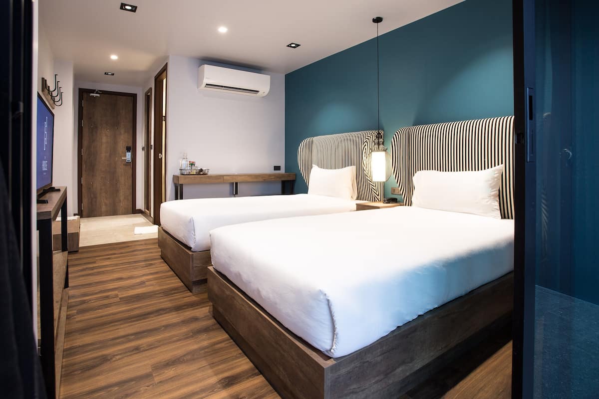 Habitación de hotel con dos camas, piso de madera, escritorio con silla y una pared azul decorativa.