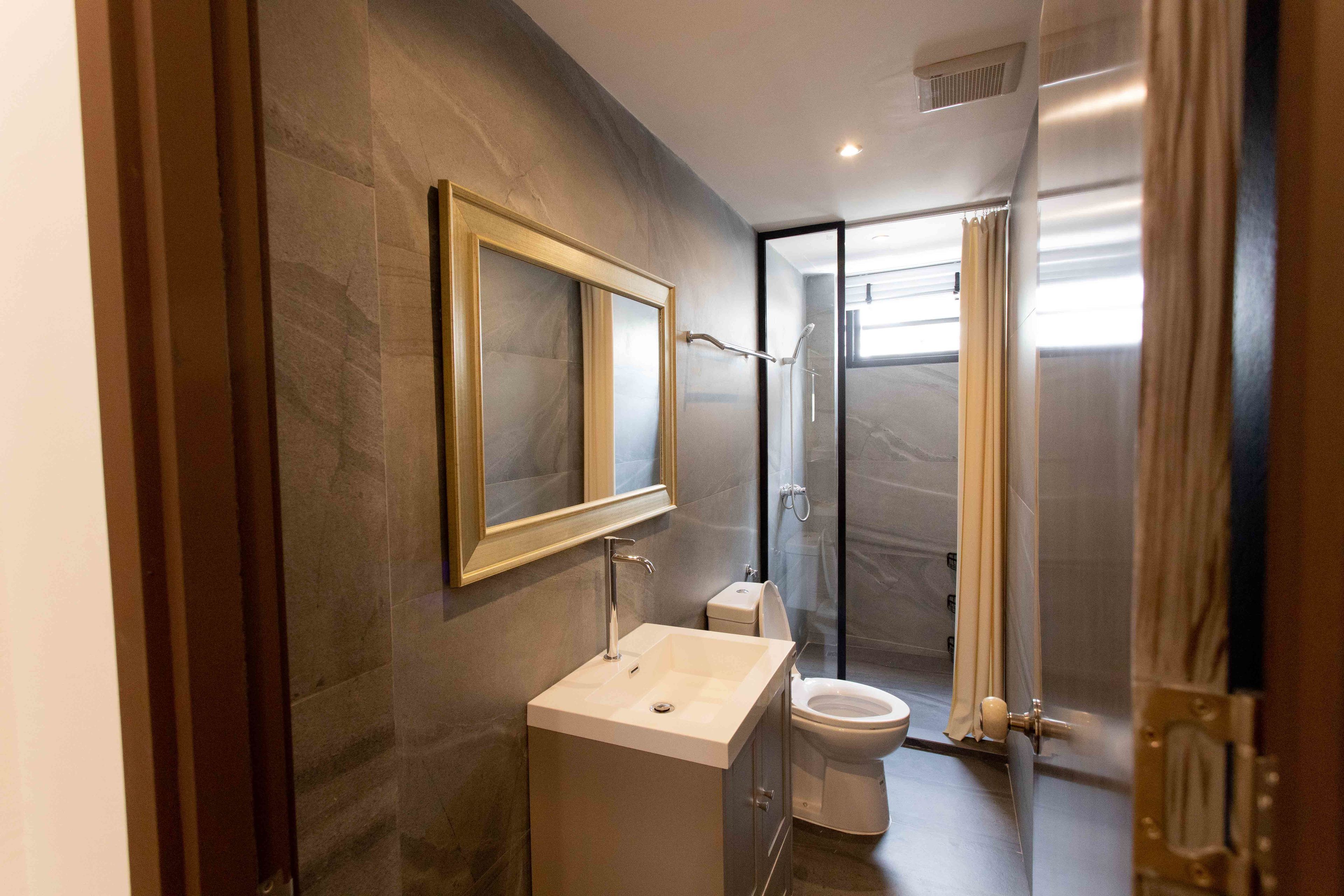 Un baño moderno con pared de mármol, un espejo grande, un lavamanos, inodoro y una cabina de ducha de vidrio.