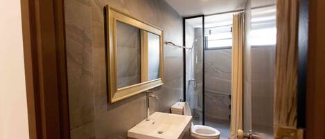 Un baño moderno con pared de mármol, un espejo grande, un lavamanos, inodoro y una cabina de ducha de vidrio.