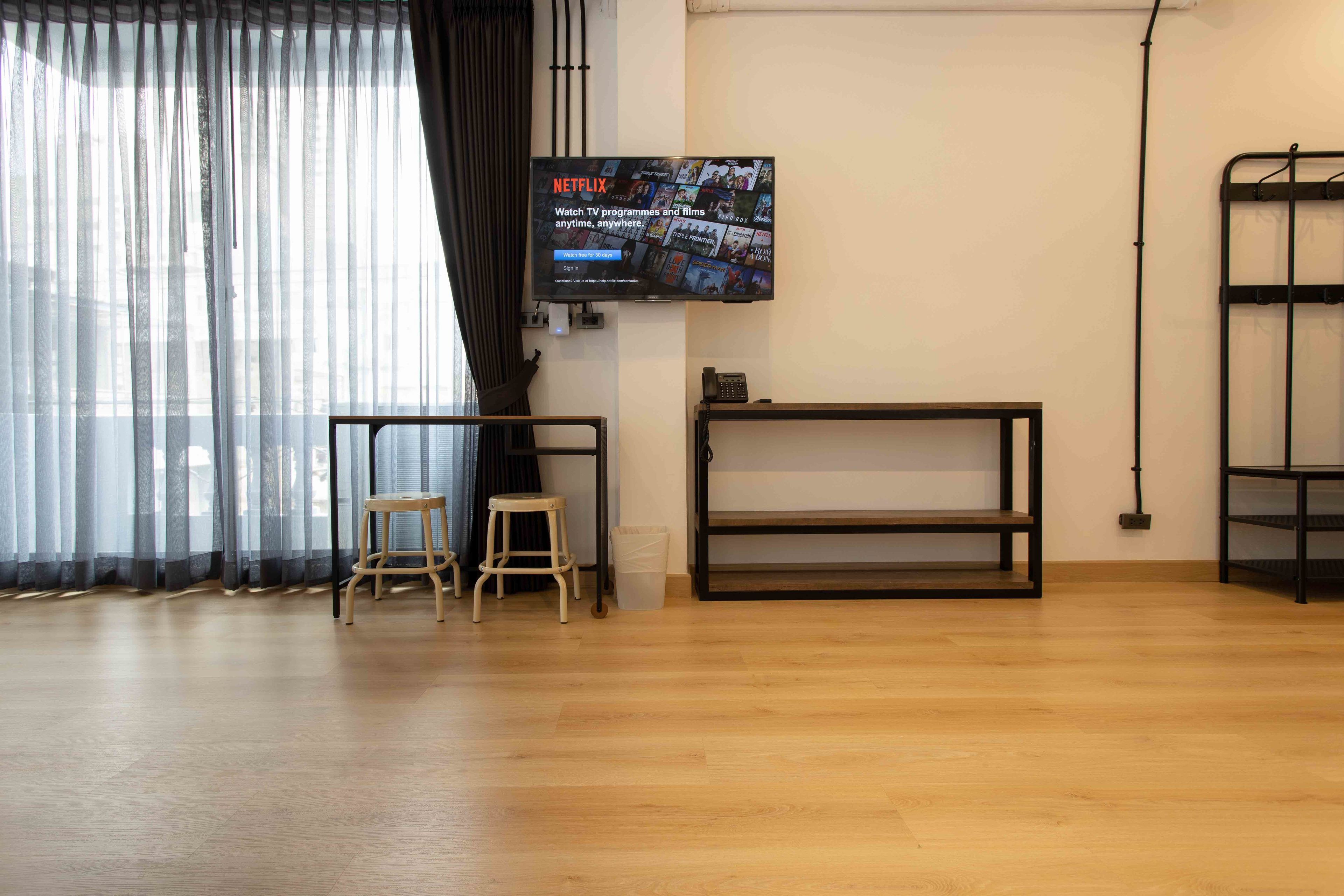Una sala de estar moderna con un televisor grande montado en la pared, piso de madera, un taburete pequeño y una estantería metálica.