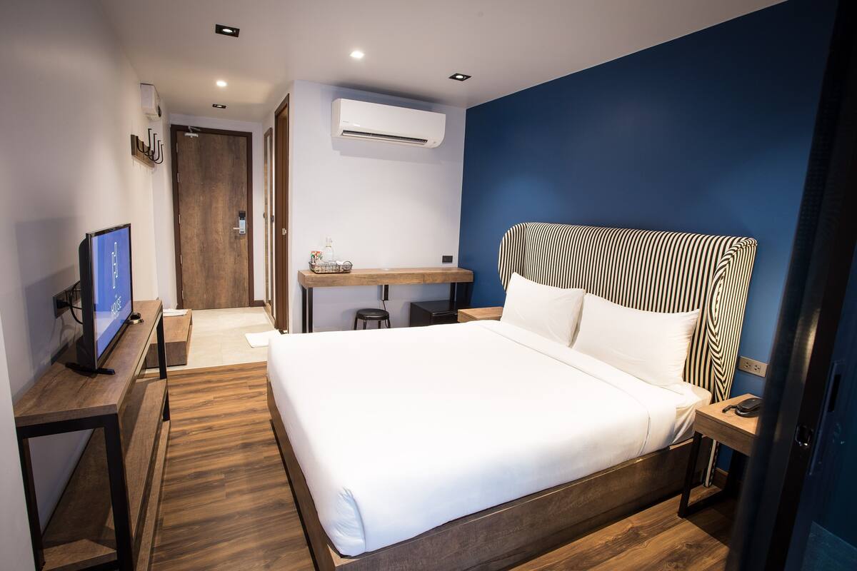 Habitación de hotel con una cama grande, un escritorio con computadora, una silla, un equipo de aire acondicionado y piso de madera.