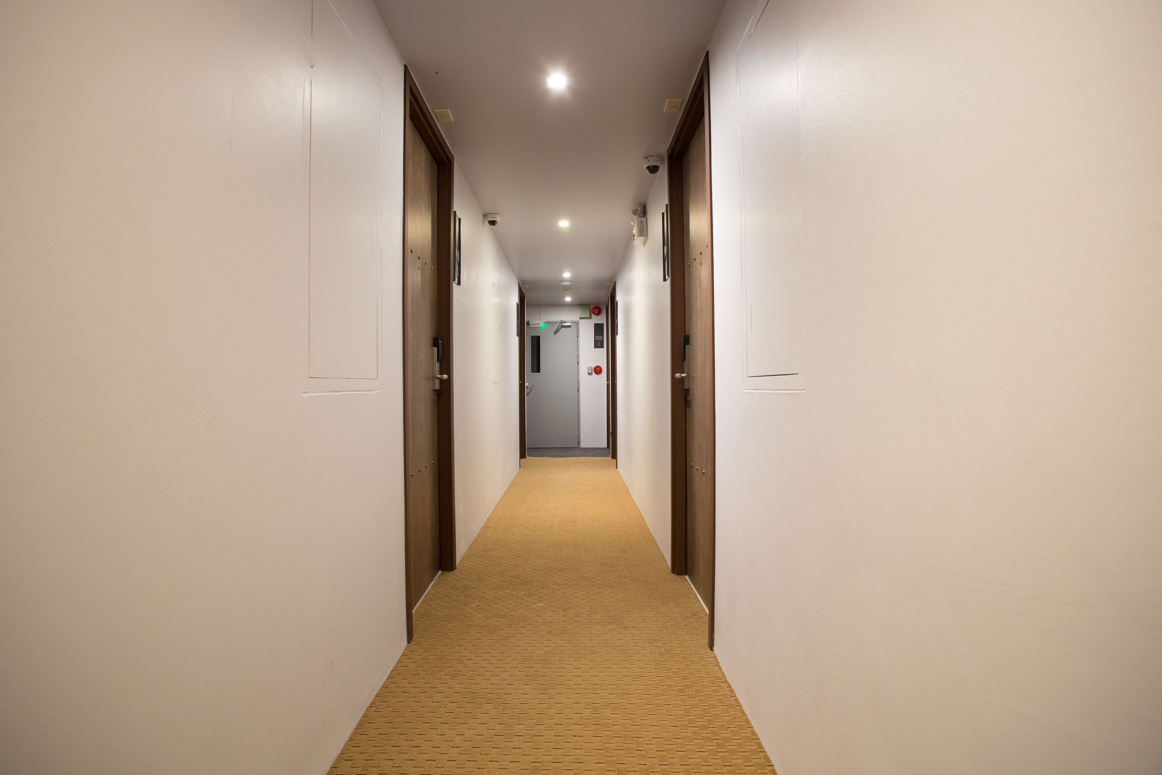 Un long couloir étroit, dont le sol est recouvert d’une moquette et où l’on trouve des portes en bois de chaque côté.
