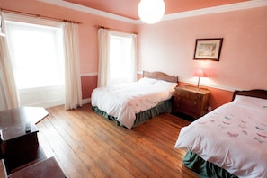 A bedroom with two beds, a dresser, a bedside lamp, and a window with curtains. - Setanta B&B (Ardee)