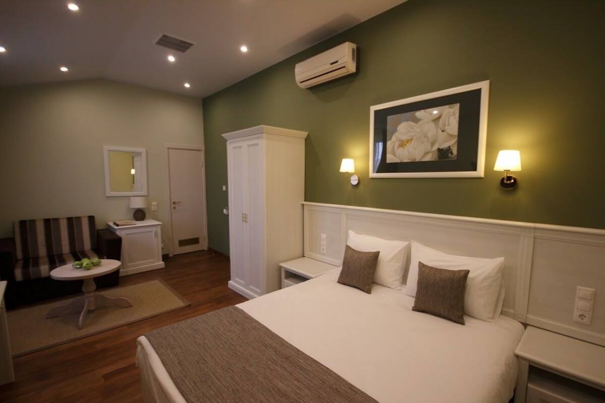 Habitación de hotel con cama, mesitas de noche, sofá, una pequeña mesa, espejo, armario y aire acondicionado instalado en la pared.