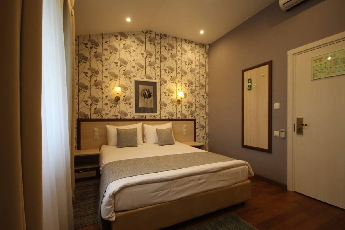 Habitación de hotel con cama, mesita de noche, un cuadro colgado en la pared y una puerta con un letrero verde.