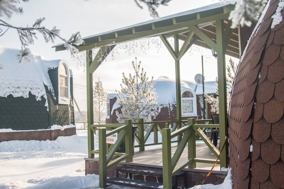 Un espacio exterior cubierto de nieve con una pérgola de madera, un banco y un letrero con el número 209.