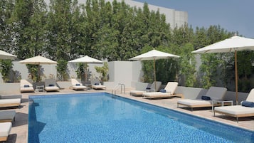 Una piscina al aire libre, sombrillas, sillones reclinables de piscina