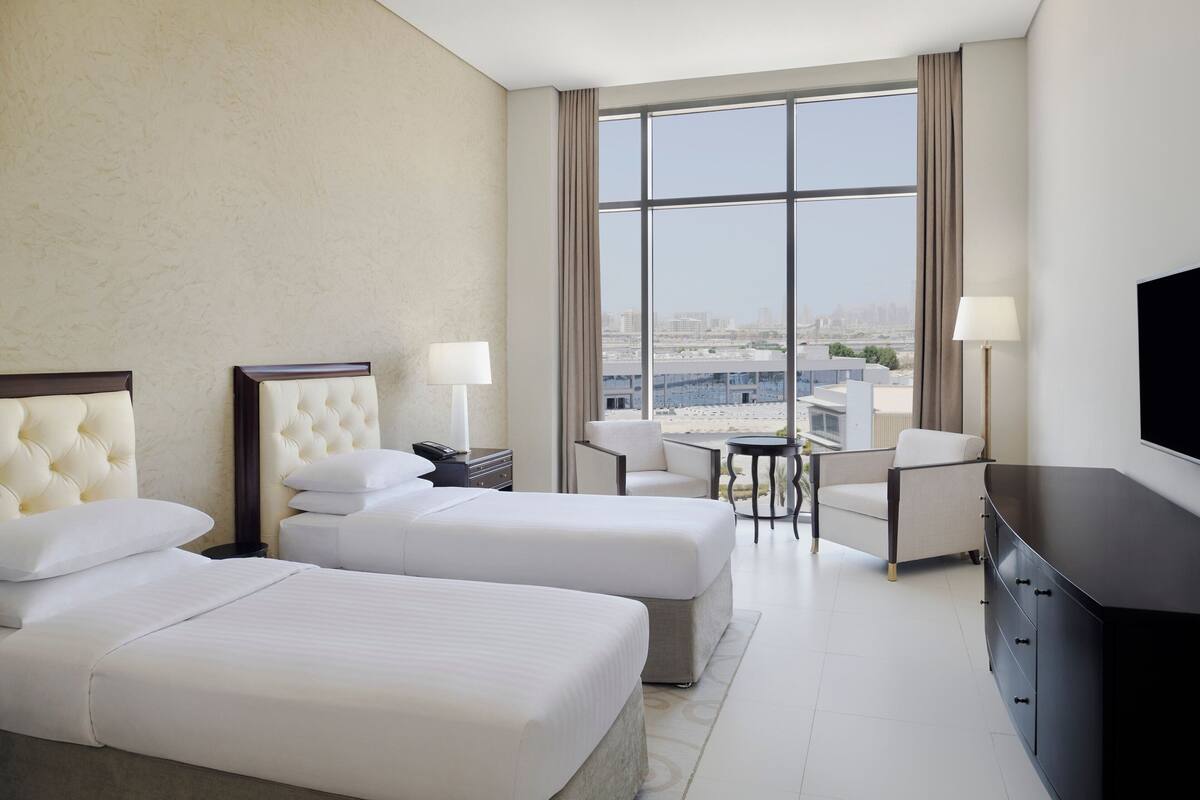 Ein Hotelzimmer mit zwei Betten, einem Fernseher, einem Schreibtisch und Blick auf die Stadt.