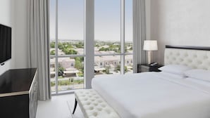 A hotel room with a large window offering a city view, a bed with white bedding, a bedside table with a lamp, and a TV on the left. - Delta Hotels by Marriott, Dubai Investment Park (Dubai)
