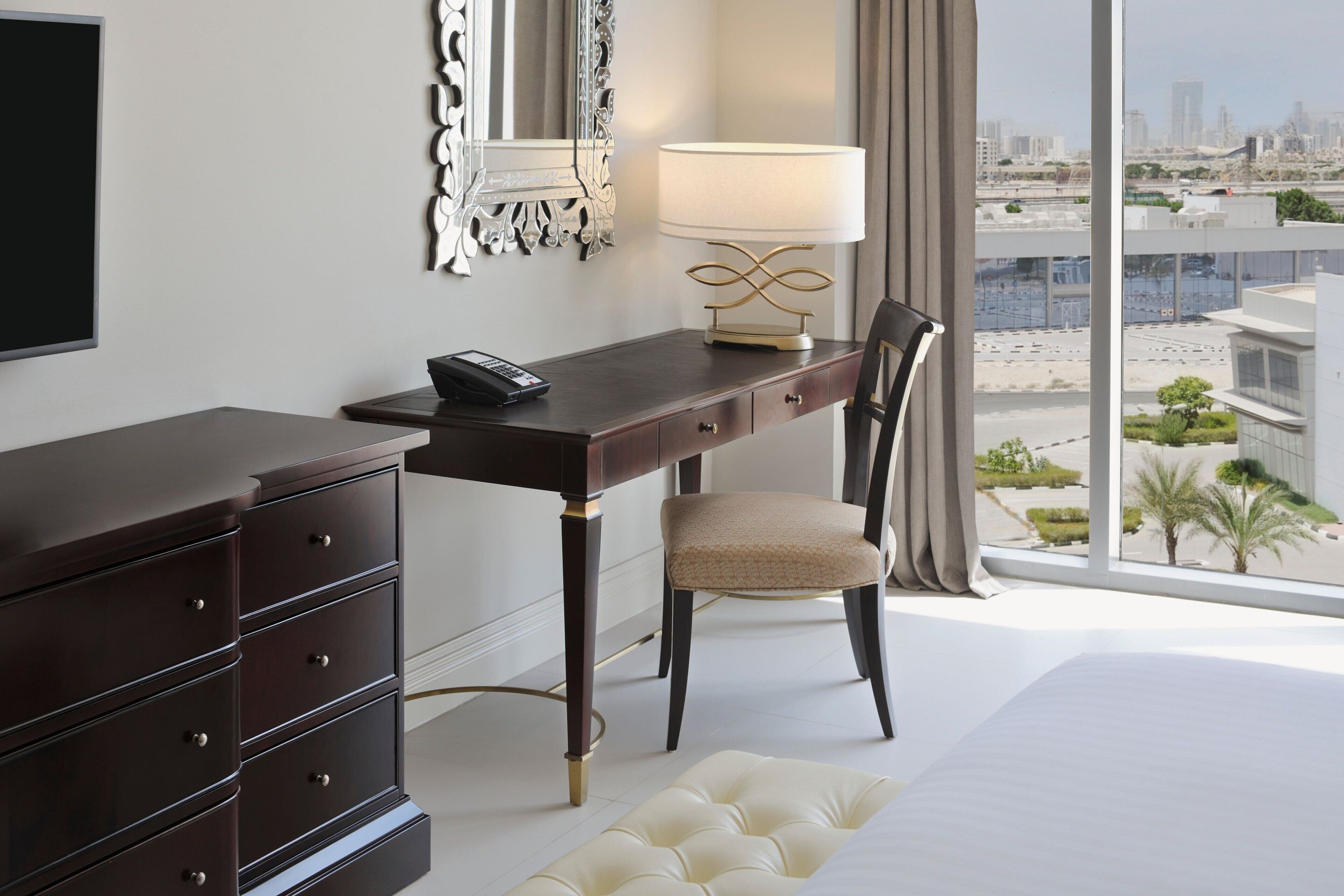 Een hotelkamer met een groot raam, een bureau met lamp, een stoel, een dressoir en een televisie.