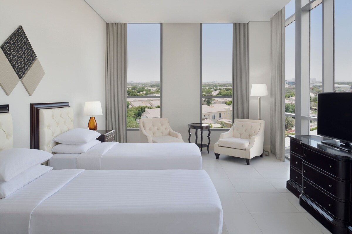 A hotel room with two beds, a TV, a dresser, and a view of the city.