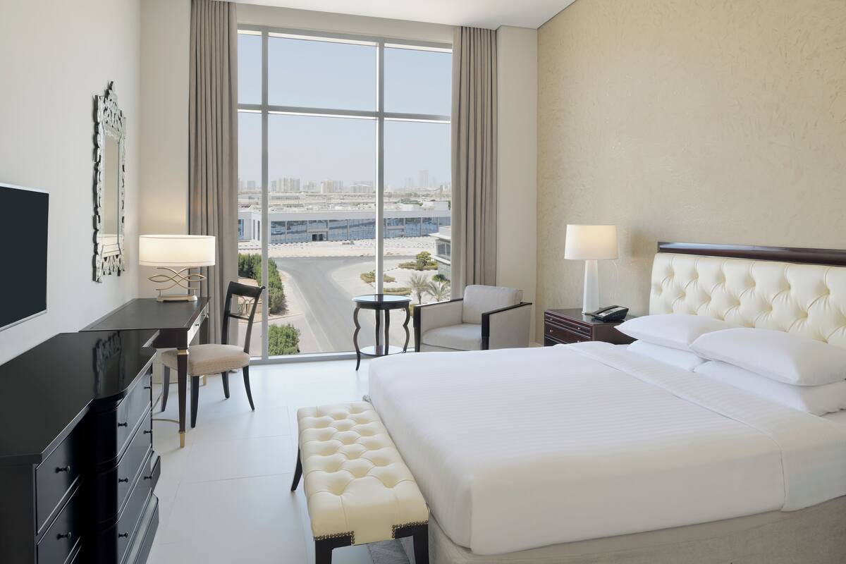 Ein Hotelzimmer mit einem großen Bett, einem Schreibtisch mit Stuhl, einem kleinen Tisch und einem Fernseher.