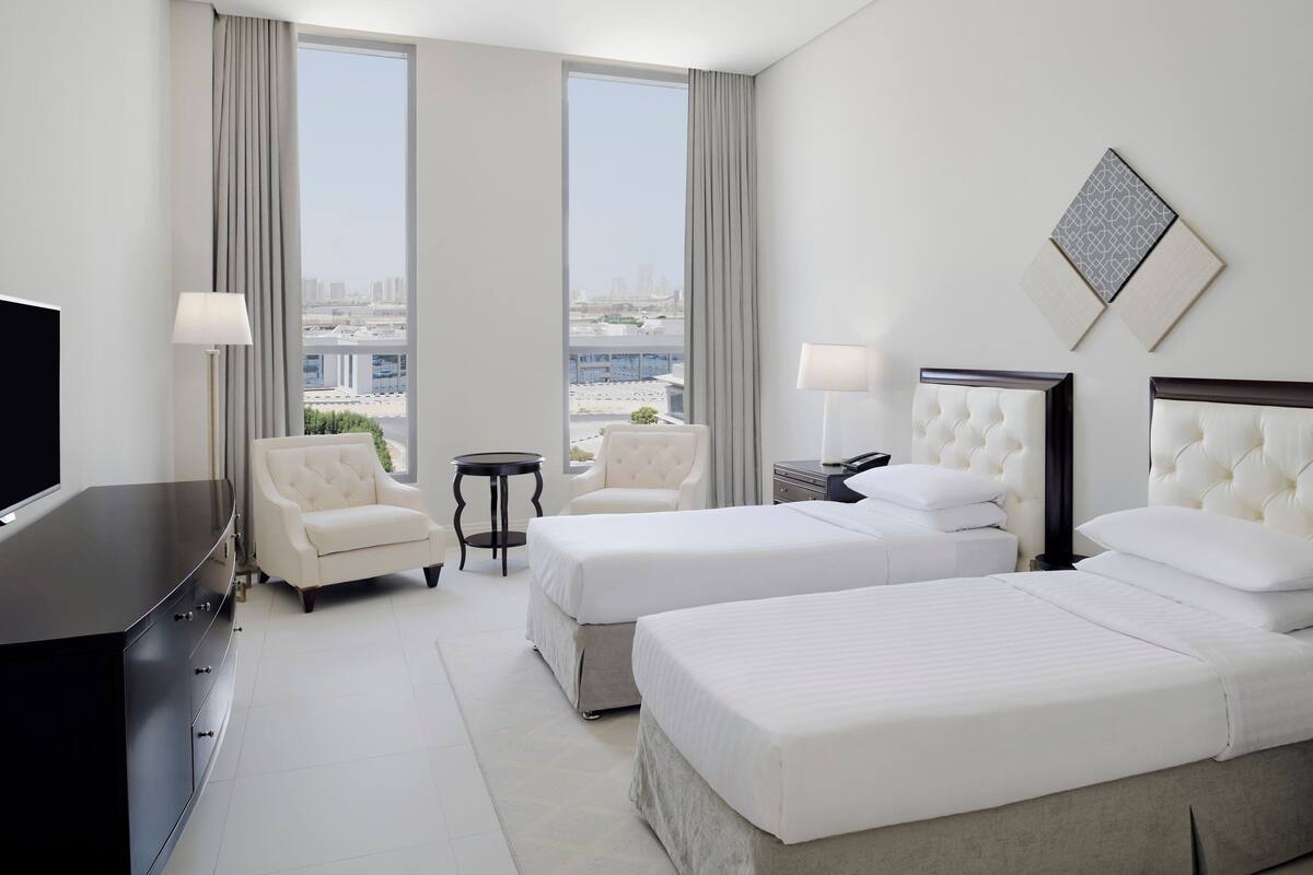Ein Hotelzimmer mit zwei Betten, einem Fernseher, einem Schreibtisch und einem Stuhl.