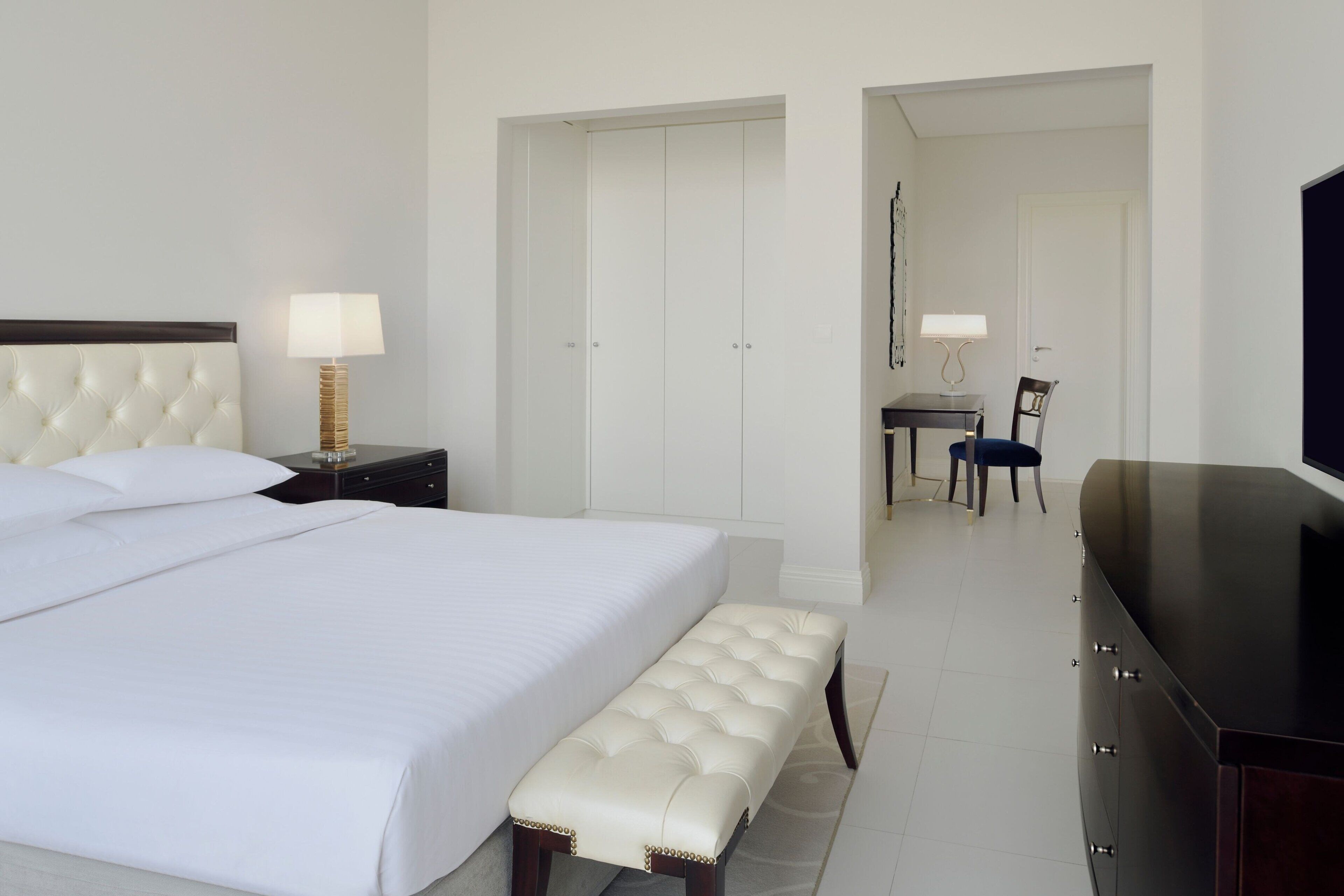Habitación de hotel con una cama grande, un banco, un aparador, un escritorio con silla y un televisor.