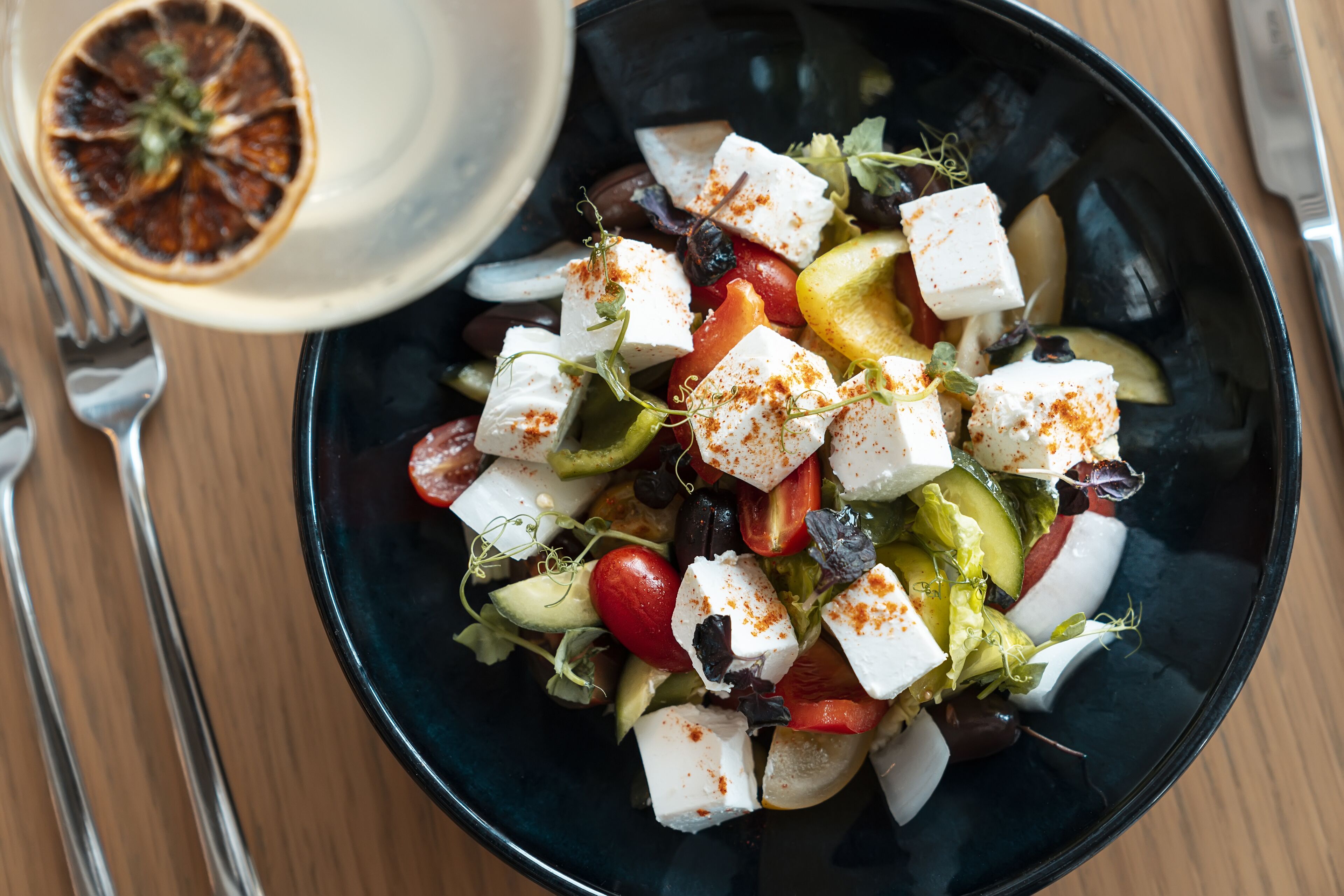A bowl of salad with feta cheese, tomatoes, cucumbers, and olives.