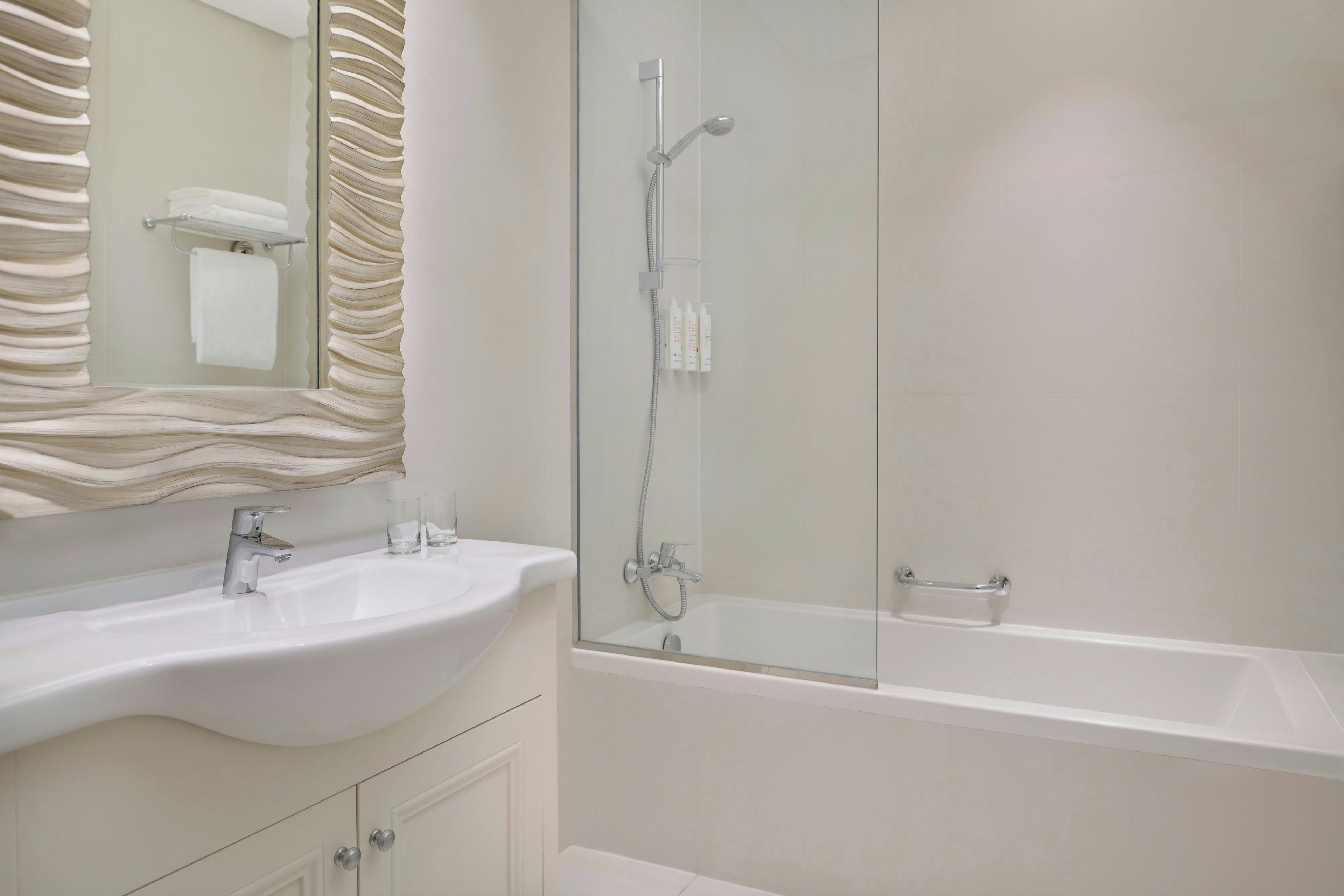 Een moderne badkamer met een wit wastafelmeubel, een glazen douchecabine en een bad.