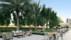 An outdoor patio area with round tables, chairs, and sofas, surrounded by palm trees and greenery. - Delta Hotels by Marriott, Dubai Investment Park (Dubai)