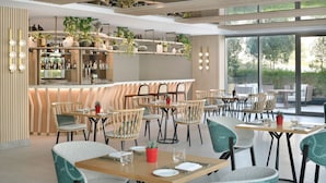 A modern restaurant with wooden tables and chairs, a bar area with shelves of bottles, and large windows offering a view of the outdoors. - Delta Hotels by Marriott, Dubai Investment Park (Dubai)