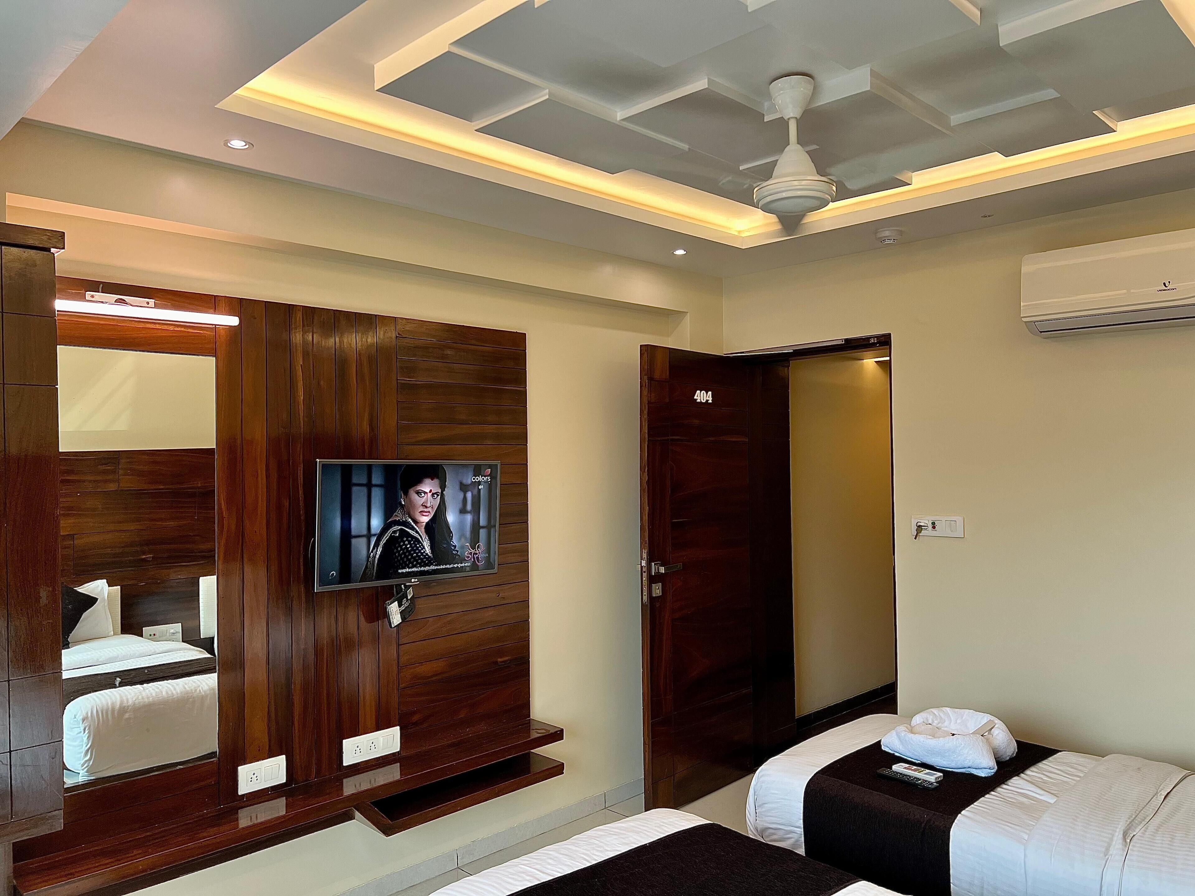 A hotel room with a wooden wardrobe, a television, a bed, and a ceiling fan.