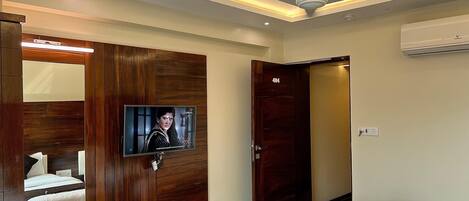 A hotel room with a wooden wardrobe, a television, a bed, and a ceiling fan.