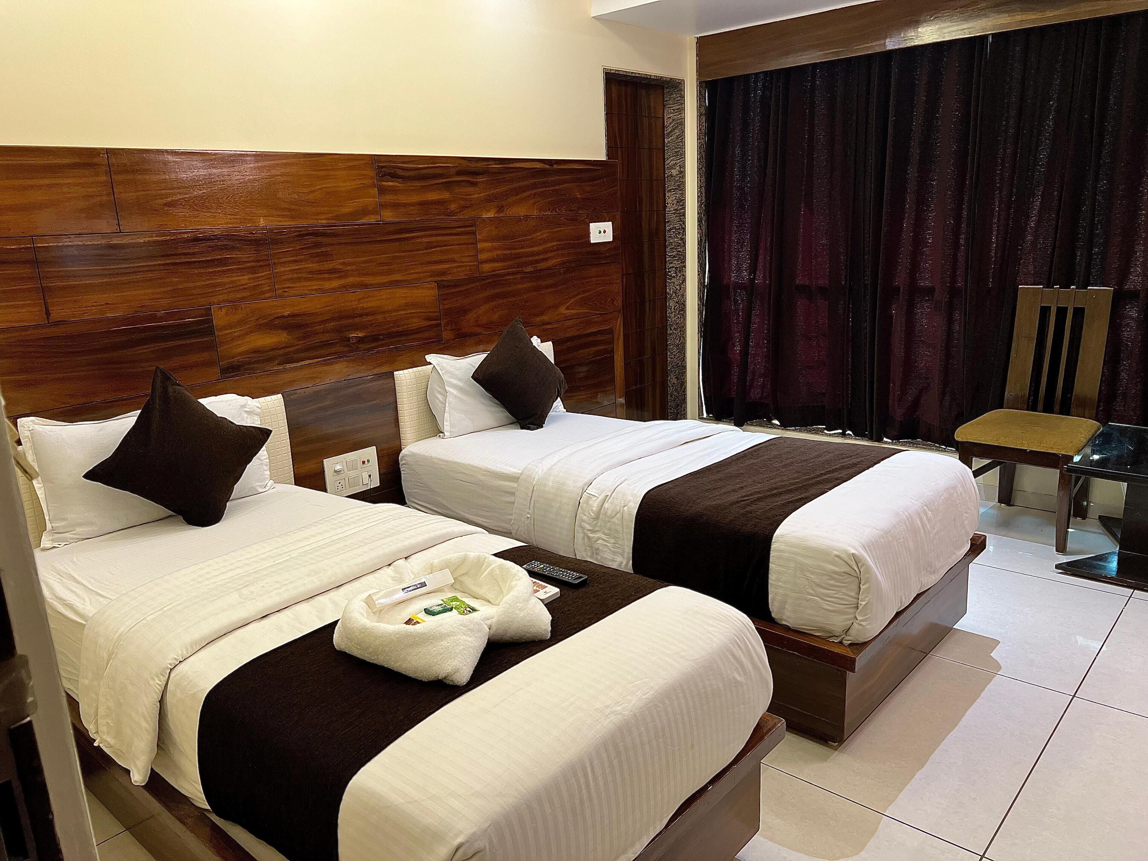 A hotel room with two beds, wooden headboard, dark curtains, and a small table with a chair.