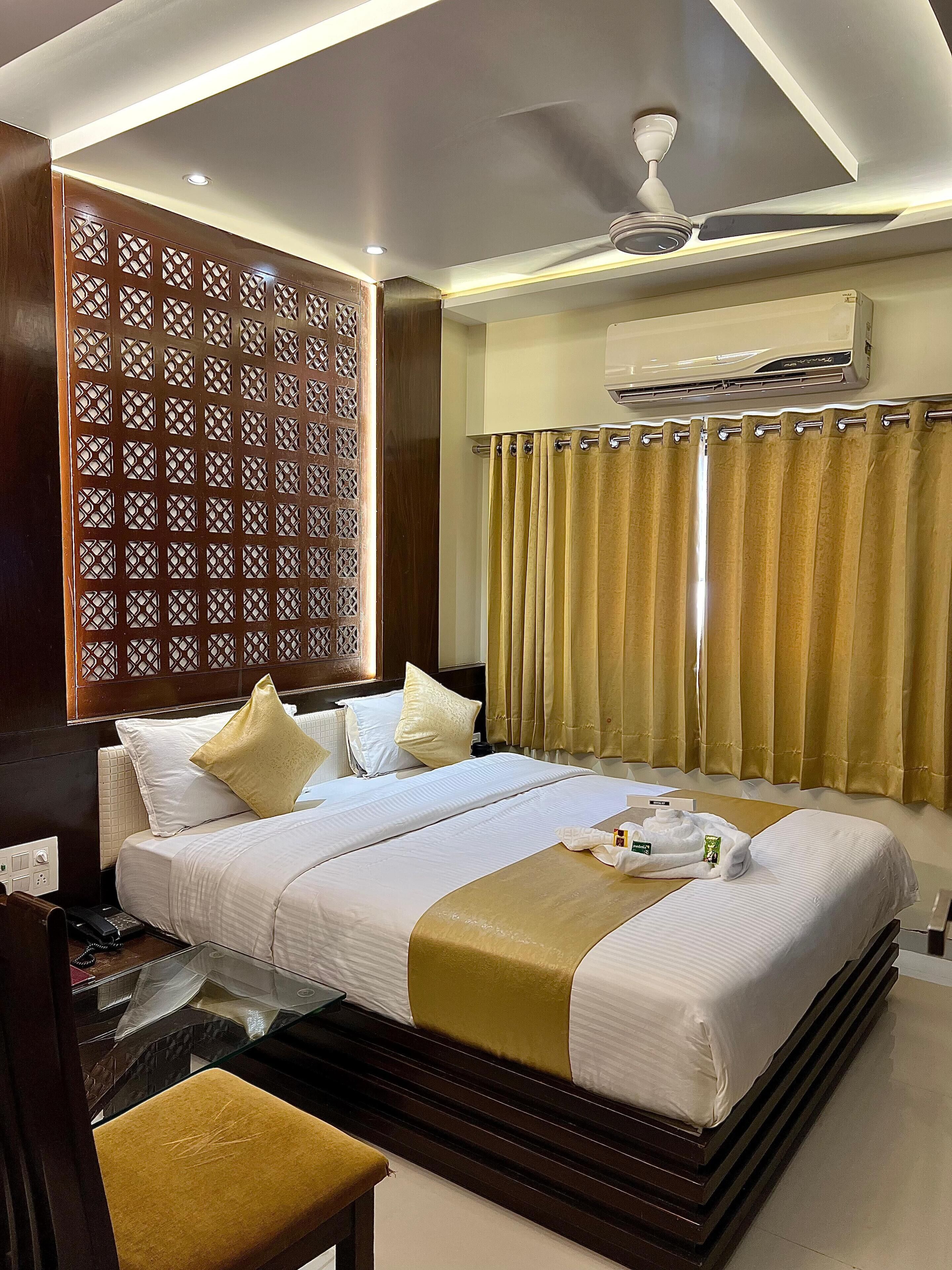 A hotel room with a large bed, a wooden headboard, a ceiling fan, and a window with curtains.
