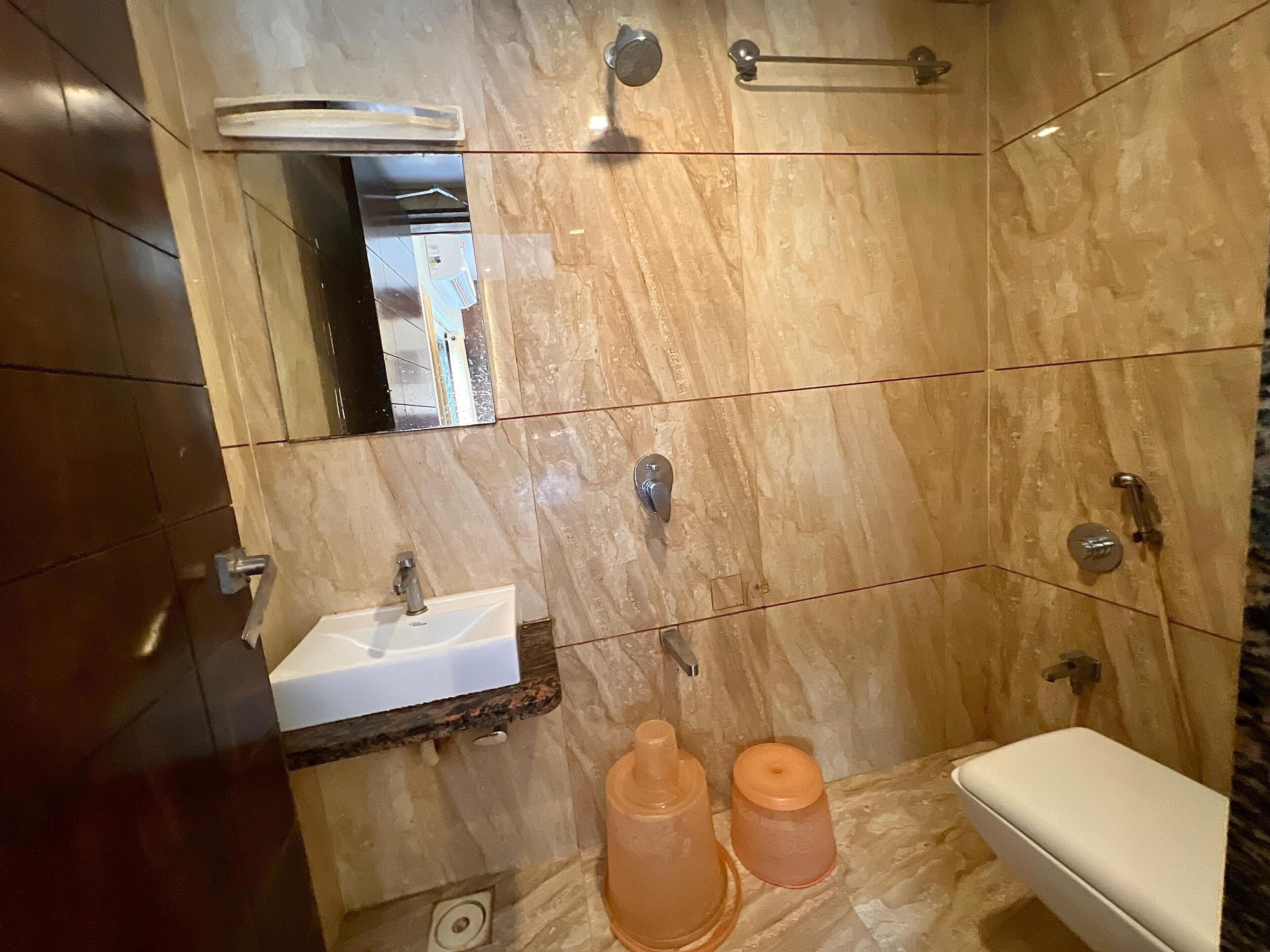 A bathroom with a marble wall, a sink, a toilet, and a shower.