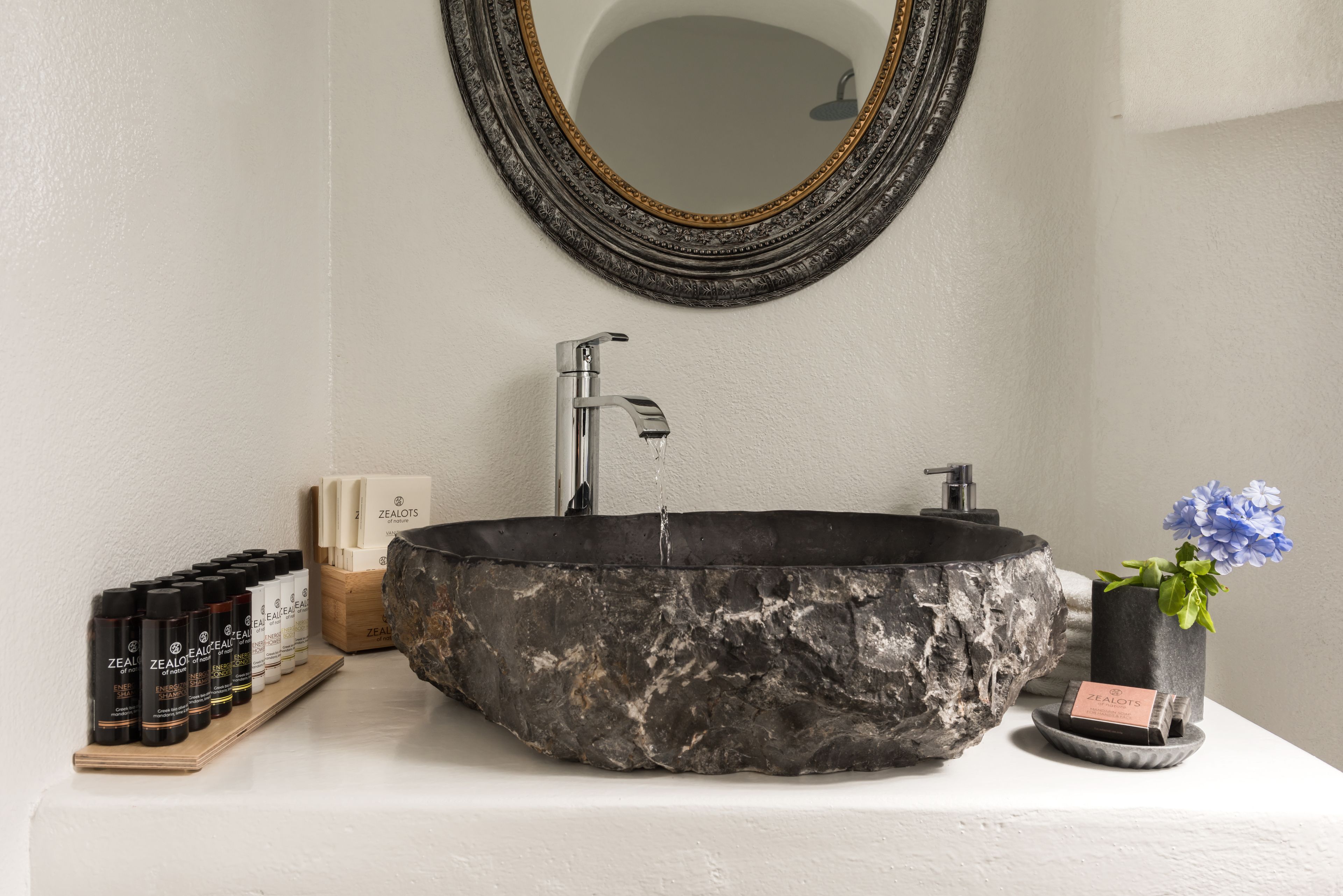 Ett badrum med ett stort handfat i natursten, en modern blandare och en spegel med en utsmyckad ram.