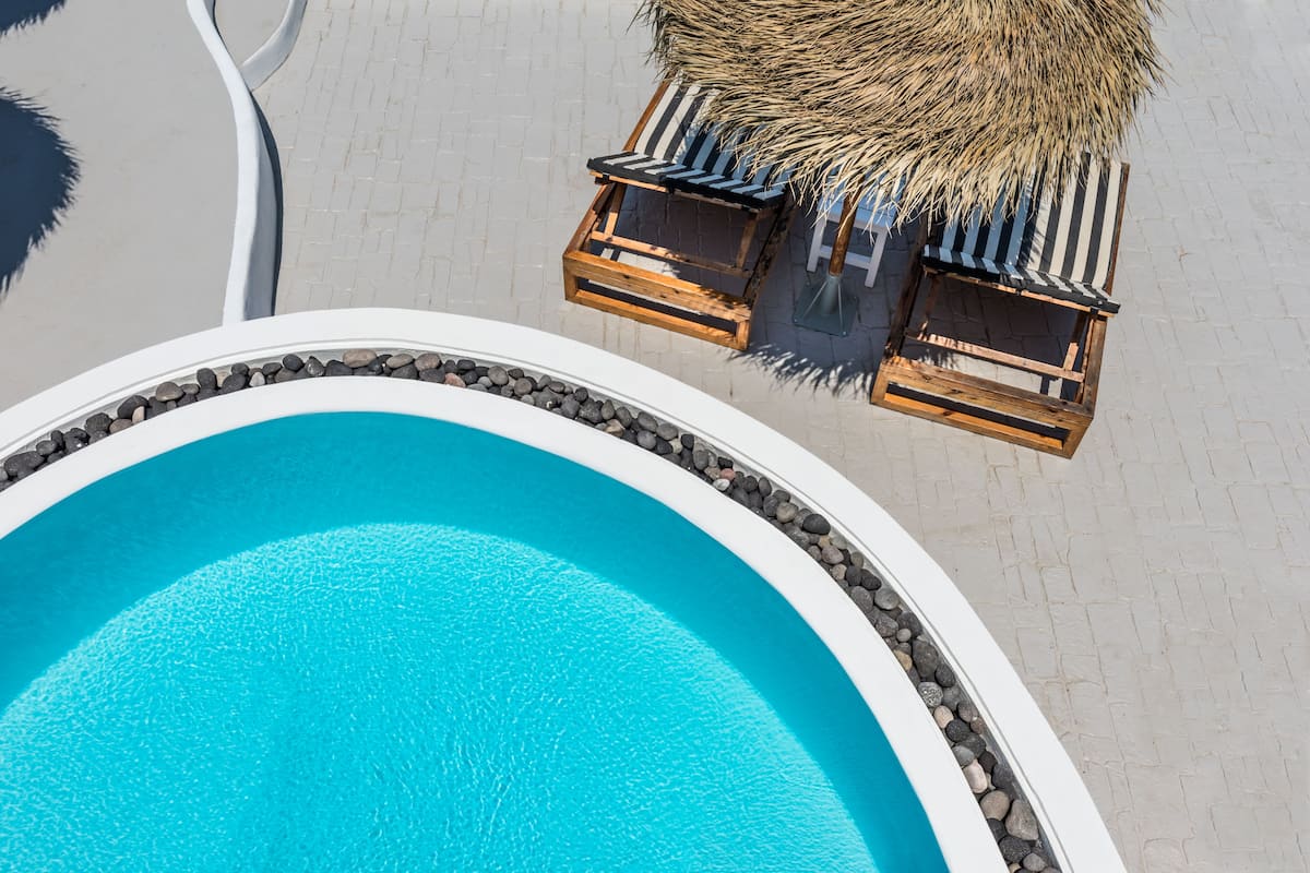 A swimming pool with a thatched roof and wooden lounge chairs.