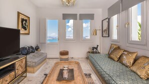 A living room with a sofa, a coffee table, a TV, and a large window with a view. - Summer Lovers Villa (Santorini)