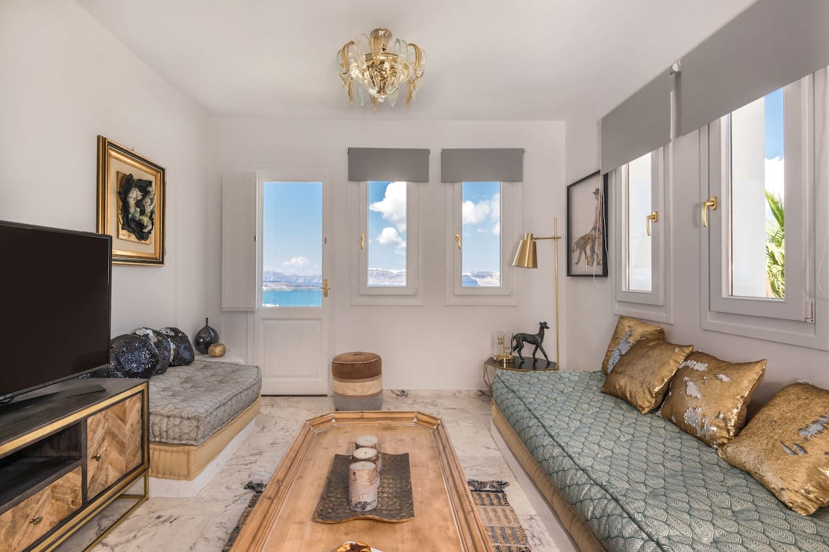 A spacious living room with a large flat-screen TV, a sofa, a coffee table, and a view of the sea through large windows.