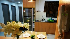 A dining area with a wooden table, a vase of white flowers, and a kitchen in the background. - Greenfield Residence Kota Kinabalu (Kota Kinabalu)