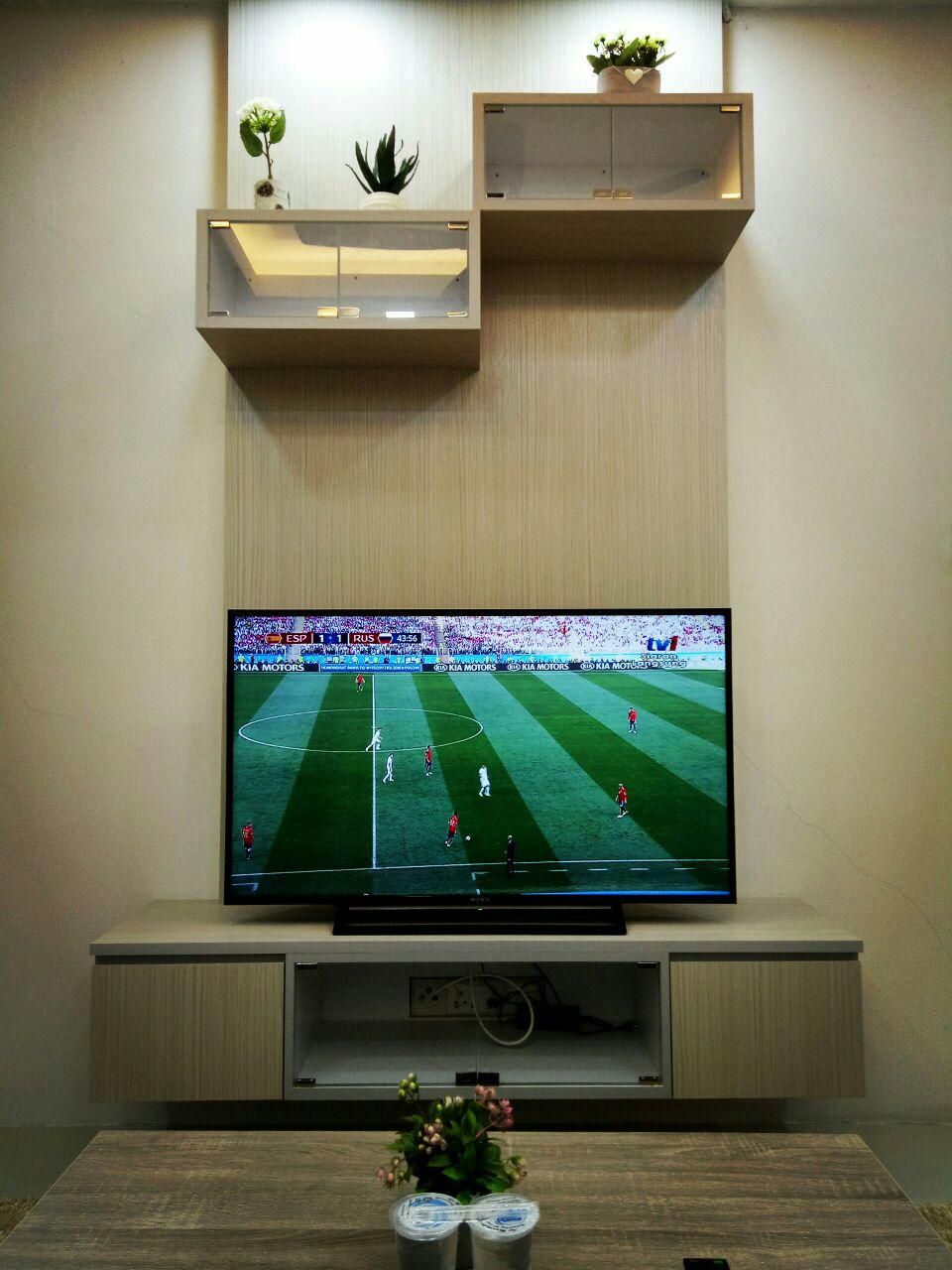 A flat-screen TV mounted on a wooden entertainment unit with a shelf above it.