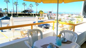 Ein Balkon mit Tisch und Stühlen, einem gelben Sonnenschirm und Blick auf das Meer und Palmen.