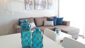 Ein modernes Wohnzimmer mit einem braunen Sofa, blau-weißen Kissen und zwei türkisblauen Glasvasen auf einem weißen Tisch.