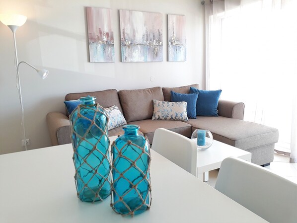A modern living room with a brown sofa, blue and white cushions, and two turquoise glass vases on a white table.