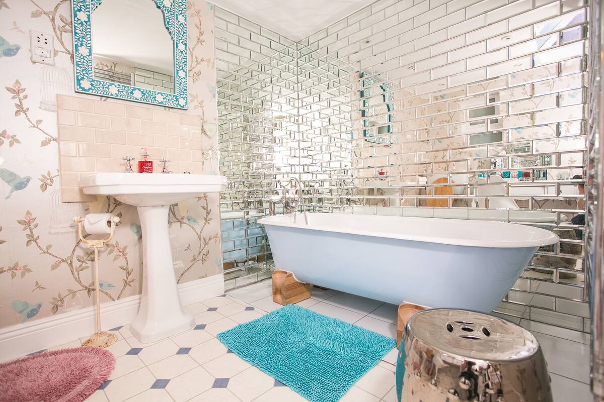 Un baño con una bañera independiente, un lavamanos pedestal y un espejo con motivos florales.