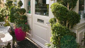 Fachada de hotel blanca, con amplias ventanas y varios topiarios en macetas.