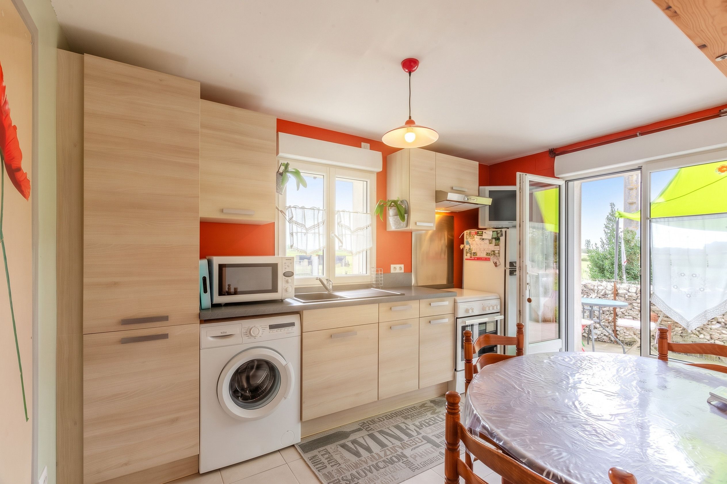 A compact kitchen with a washing machine, microwave, and a dining area with a table and chairs.
