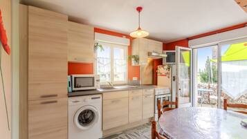 A compact kitchen with a washing machine, microwave, and a dining area with a table and chairs.