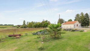 Un paysage rural avec un bâtiment blanc doté d’un toit rouge, entouré de verdure et d’un champ.