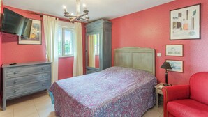 Une chambre à coucher comprenant un lit, une commode, un téléviseur, un lustre et des œuvres d’art accrochées aux murs.