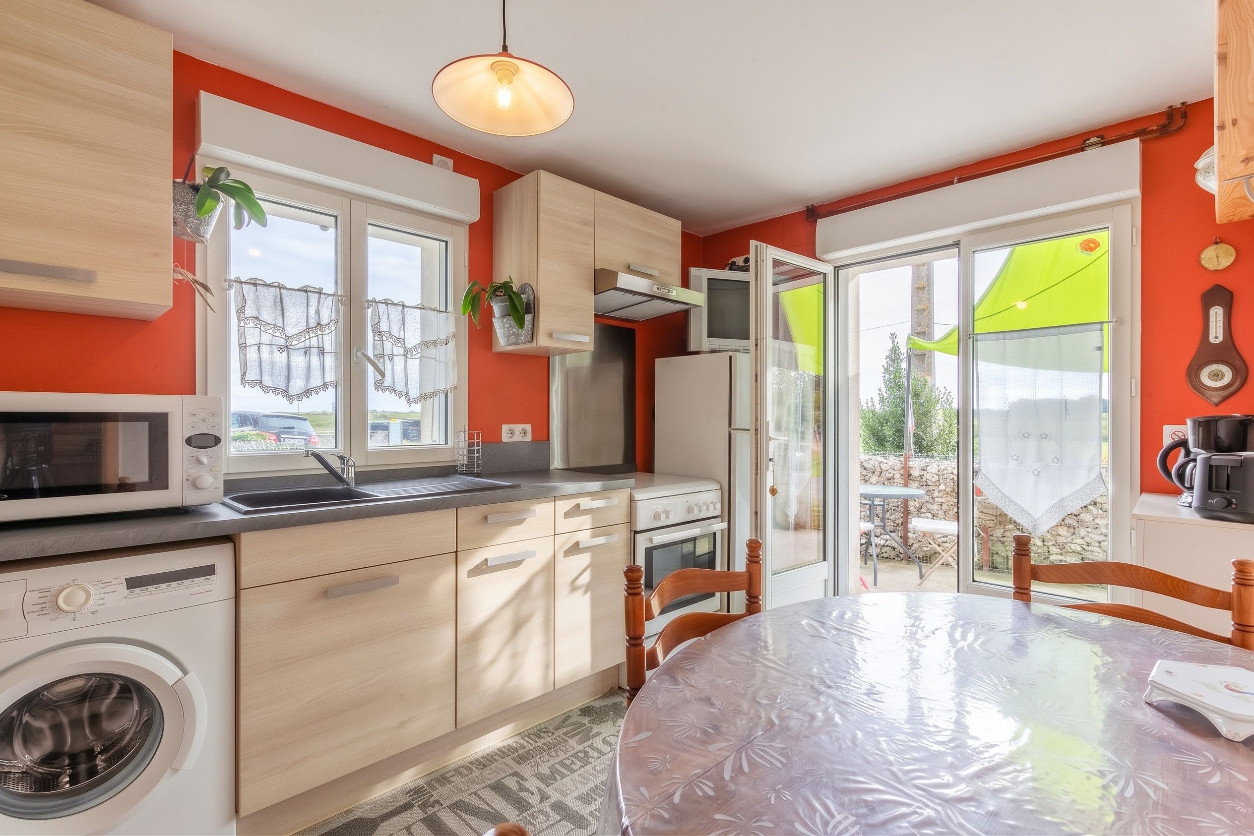 Une cuisine moderne équipée d’un lave-linge, d’un coin repas avec une table et offrant une vue sur l’extérieur.