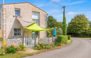 A two-story building with a stone wall foundation, a metal fence, and a green umbrella.