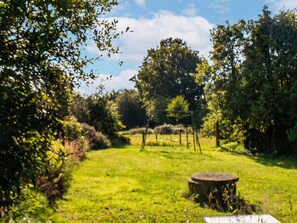 Un'area verdeggiante all'aperto con un'altalena, una struttura circolare in pietra e fitta vegetazione.