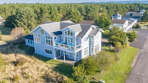 A large, two-story house with a prominent balcony, surrounded by a forested area and other residential properties. - Pets OK, Amazing View, Steps to Town & Beach (Seas) (Long Beach)