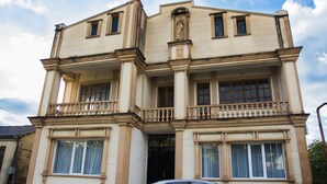 Een meerlaags gebouw met een balkon op de tweede verdieping, een auto ervoor geparkeerd en een heldere lucht erboven.