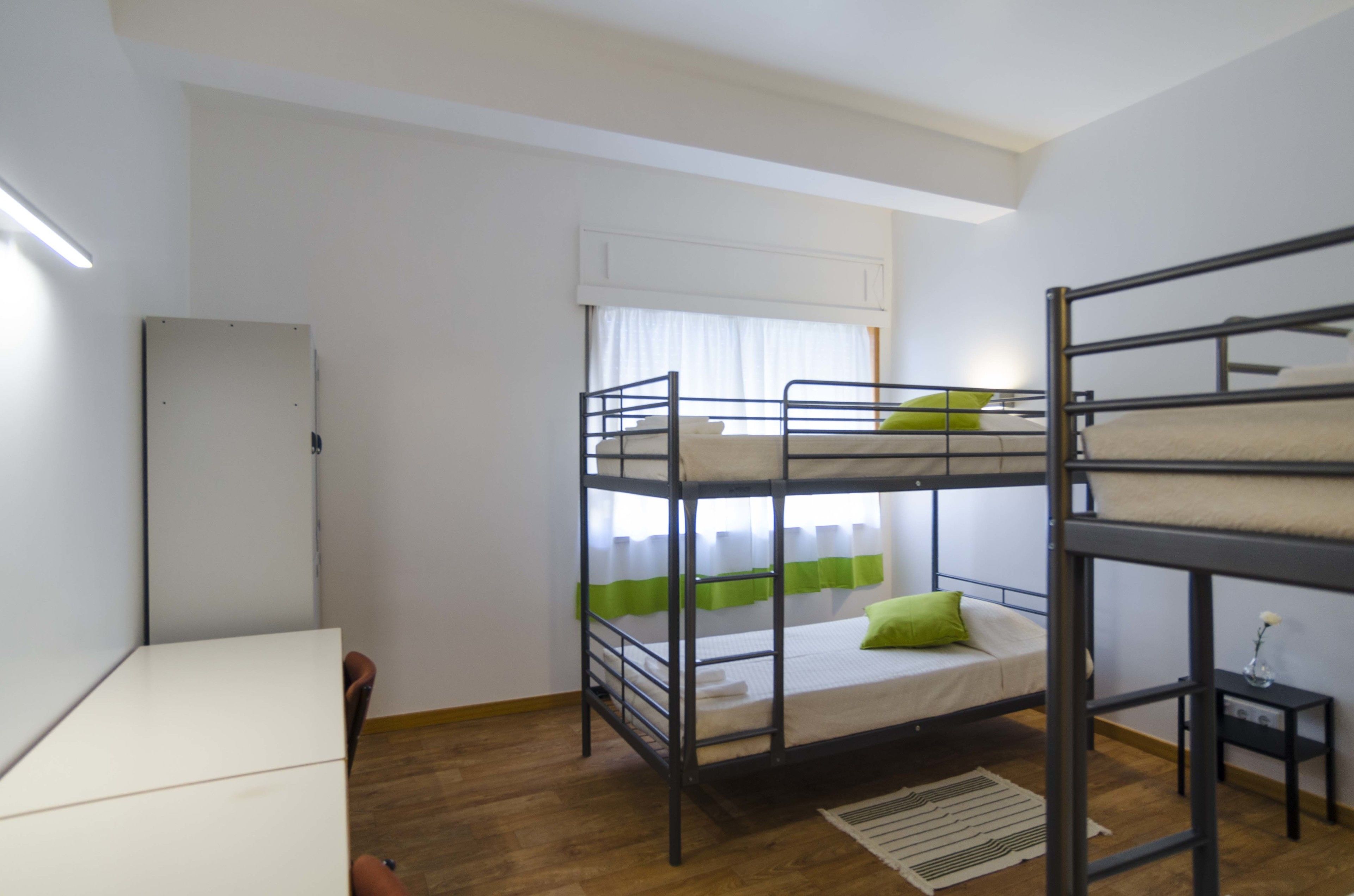 Habitación con literas, escritorio, radiador y ventana con cortinas.